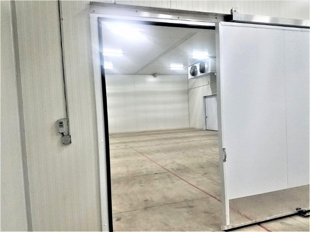 Sliding insulated door opening into a refrigerated cold room with ceiling evaporator units
